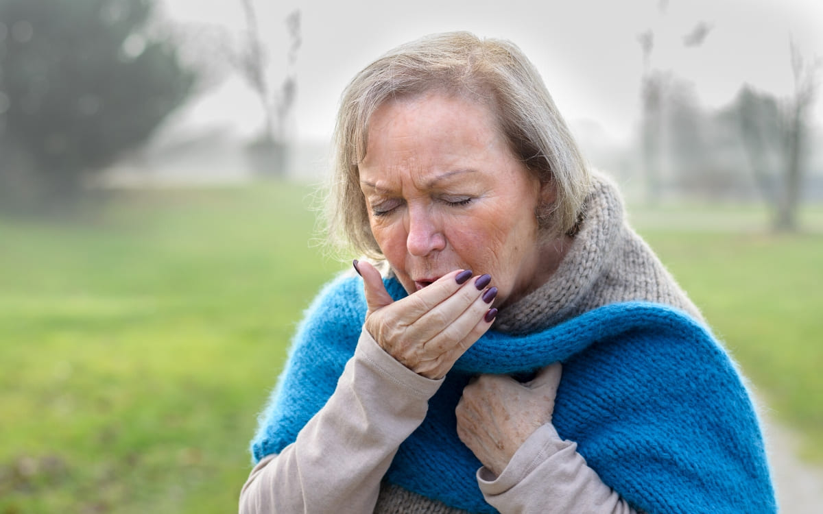 A mature woman coughing as she covers her mouth with her right hand