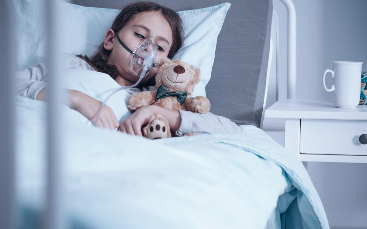 A little girl with cystic fibrosis holding her teddy bear as she lays in a hospital bed