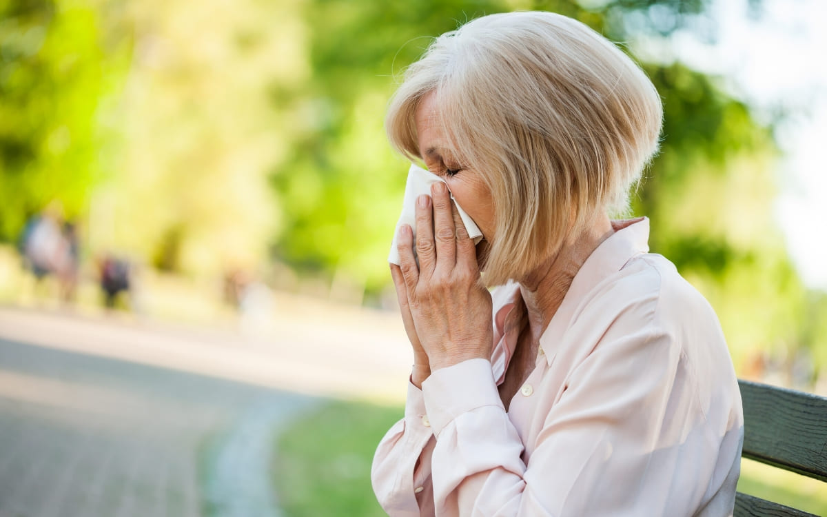 A mature woman blowing her nose as she tries to relief allergy symptoms