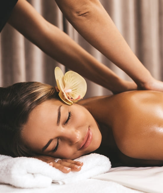 A young woman with a beautiful flower on her hair receiving a relaxing massage